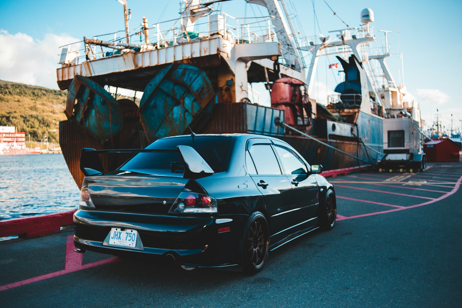 Right-hand-drive Japanese sports sedan parked on a dock beside a cargo vessel, ready for export